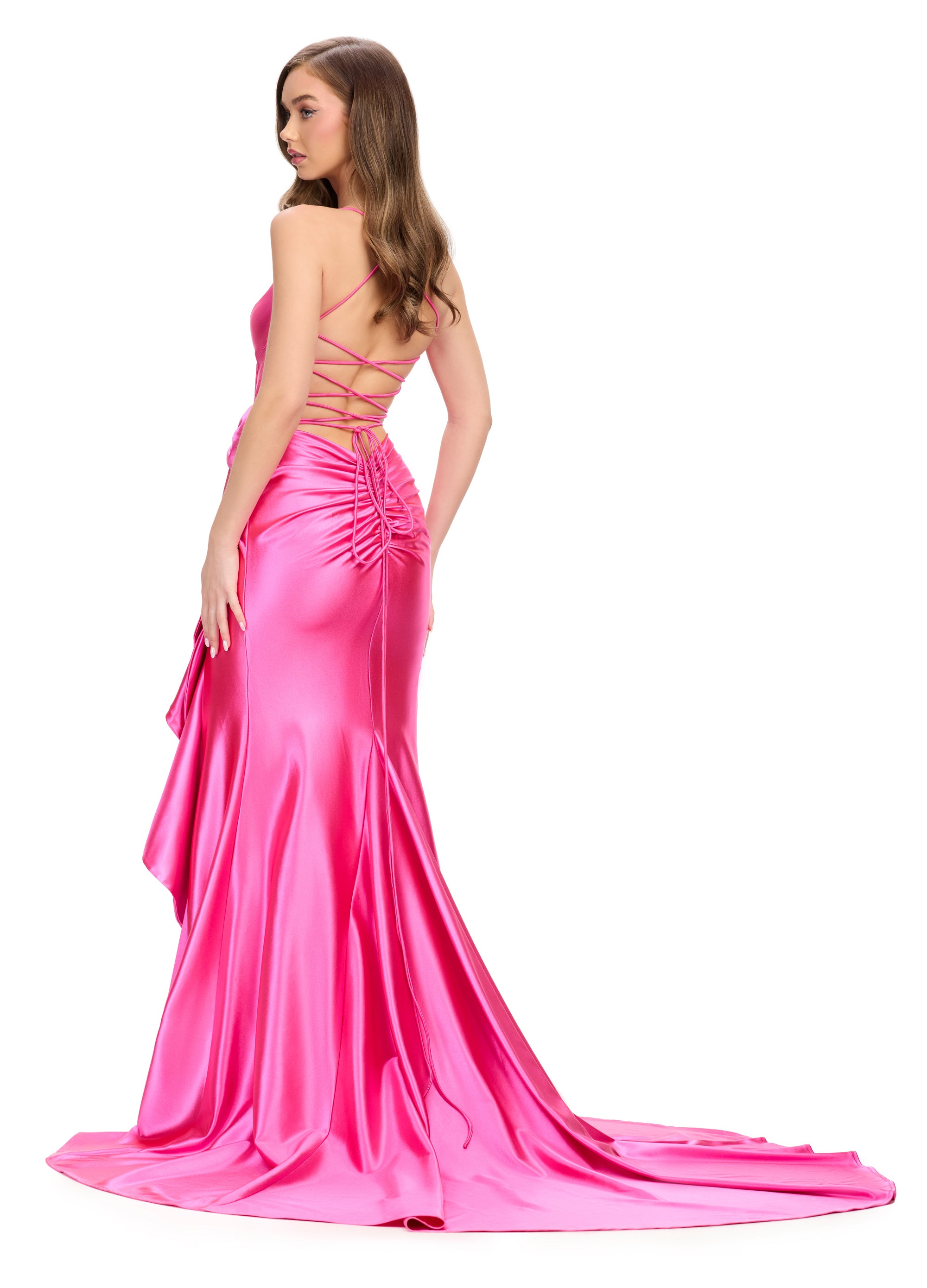 Elegant hot pink evening gown with a fitted bodice, spaghetti straps, cross back and a large bow accent at the waist. The dress features a cascading ruffle detail along the high slit and flows into a floor-length satin skirt.