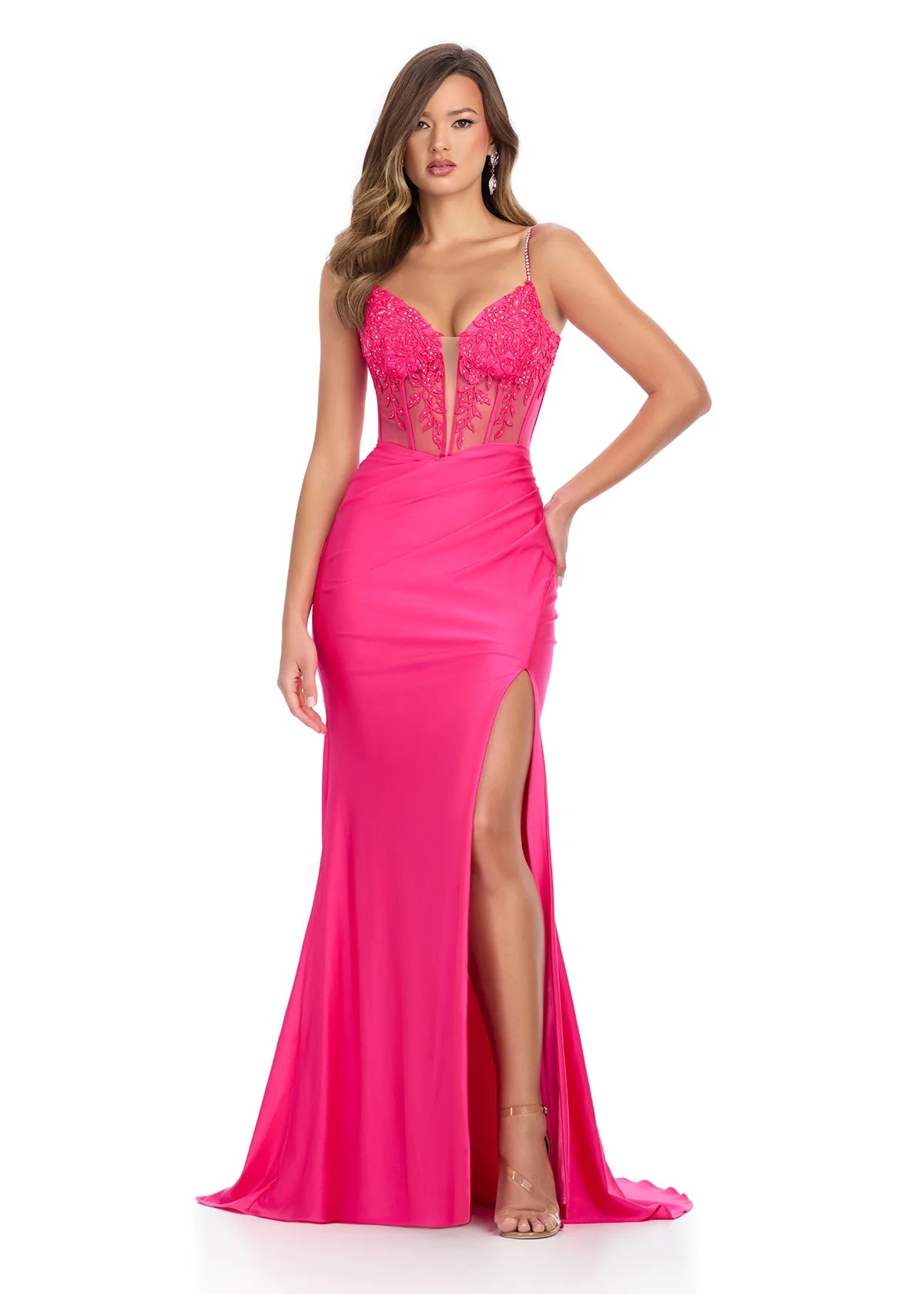 Fuchsia pink evening gown featuring a sheer illusion bodice with floral lace appliqués, thin spaghetti straps, a thigh-high slit, and a flowing floor-length skirt.