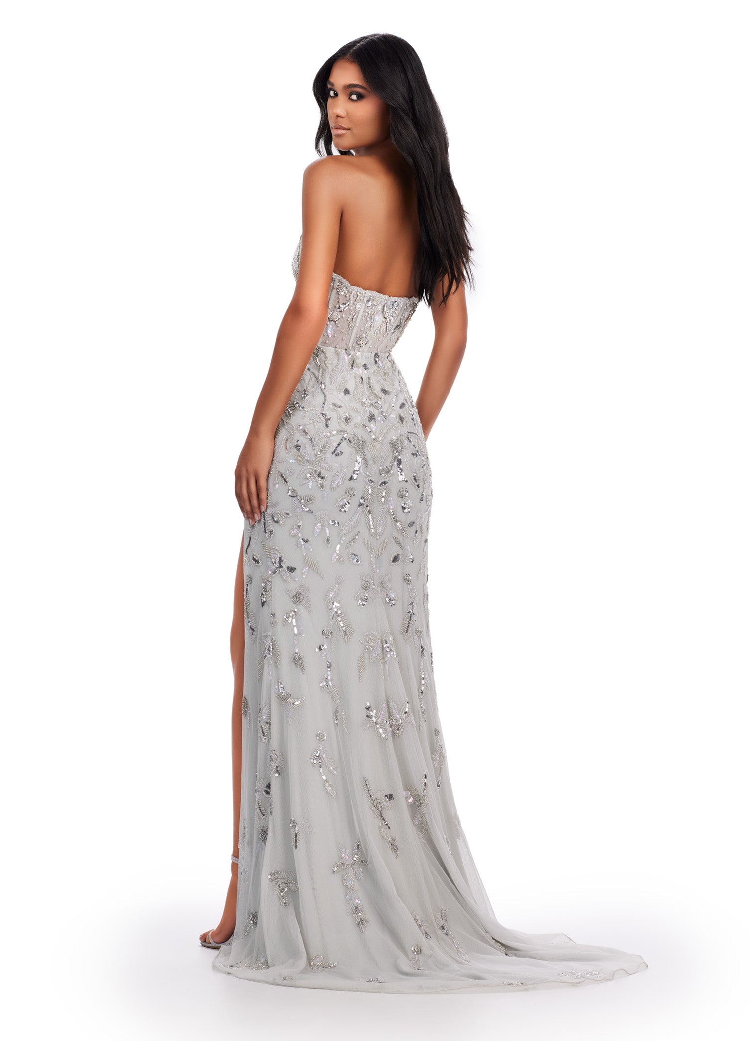 Back view of a stunning silver strapless gown adorned with intricate beaded embellishments, featuring a fitted bodice, a thigh-high slit, and a sheer overlay for a captivating and glamorous look.