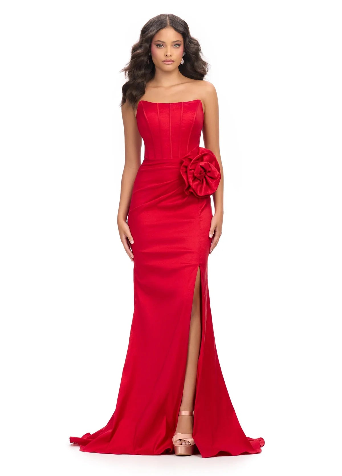 Strapless red gown with a corset-style bodice, high slit, floor-length skirt, and a large floral accent at the waist.