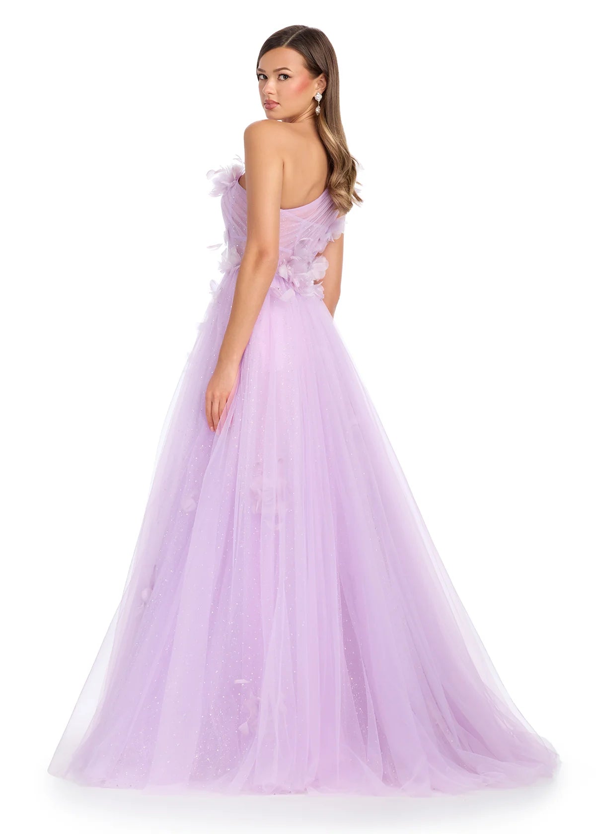 Back view of a lilac one-shoulder ball gown featuring delicate tulle layers adorned with soft floral appliqués, a semi-sheer corset bodice, and a romantic flowy skirt that glimmers subtly, perfect for an enchanting evening.