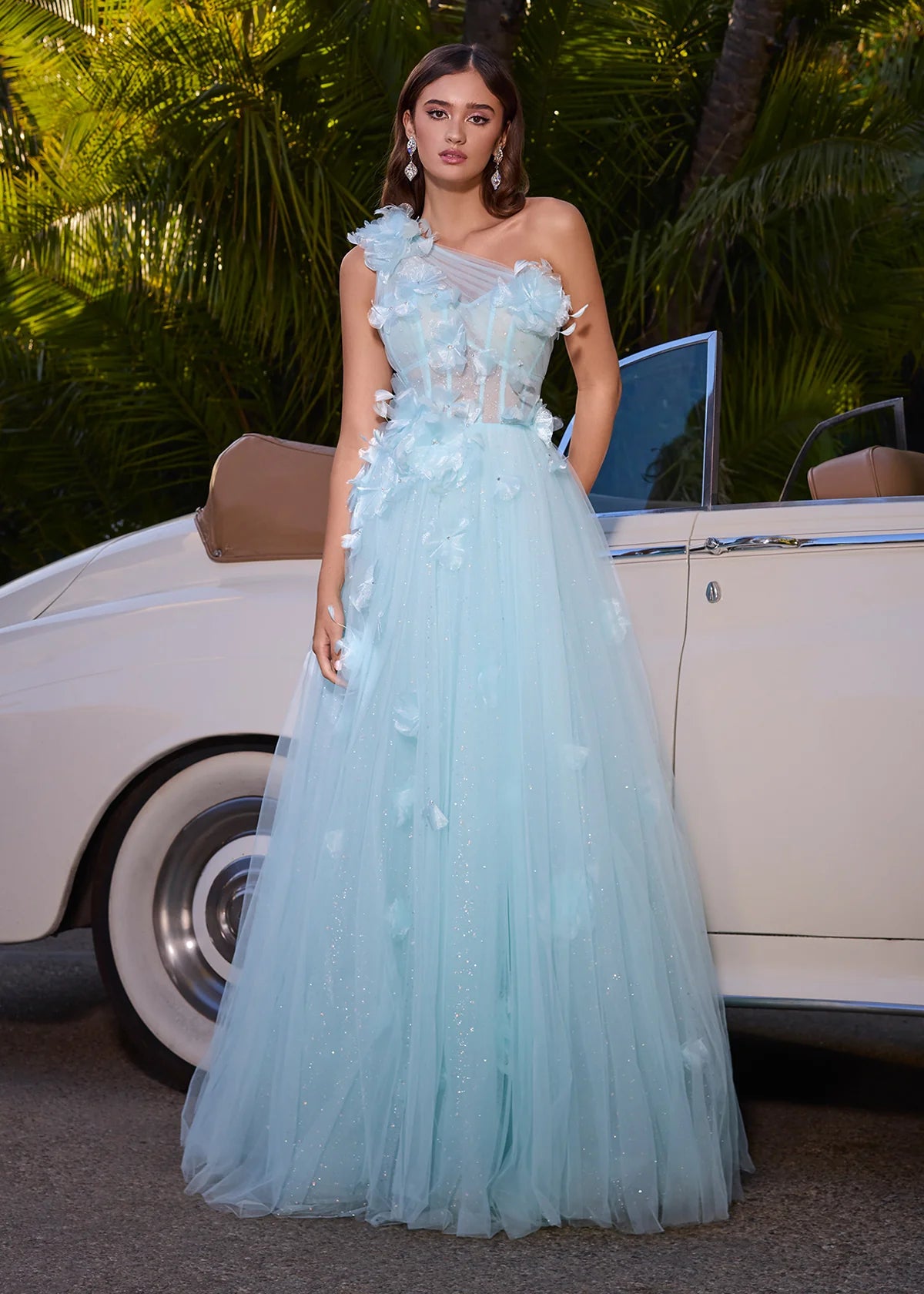 A stunning ethereal one-shoulder ball gown featuring delicate tulle layers adorned with soft floral appliqués, a semi-sheer corset bodice, and a romantic flowy skirt that glimmers subtly, perfect for an enchanting evening.