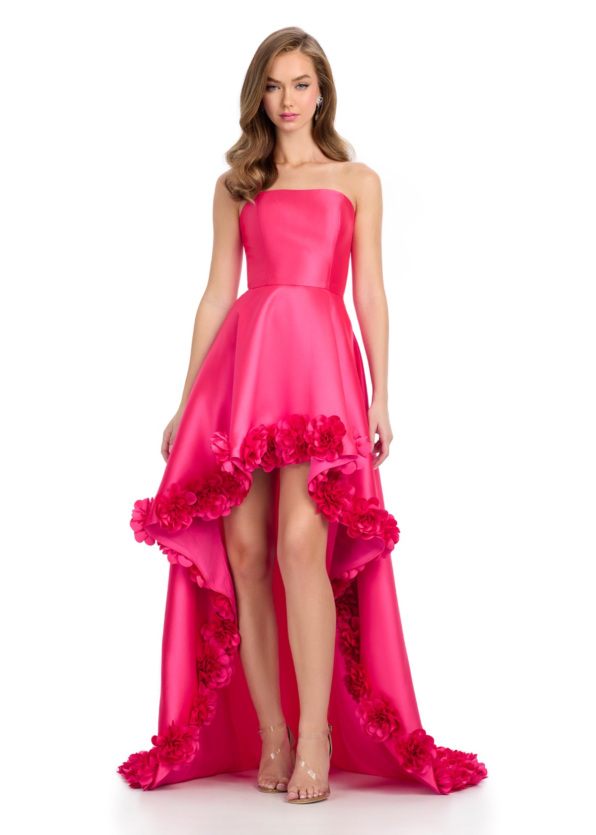 Fuchsia high-low gown with a strapless bodice, satin finish, and dramatic floral appliqué detailing along the hem, creating a bold and romantic statement.