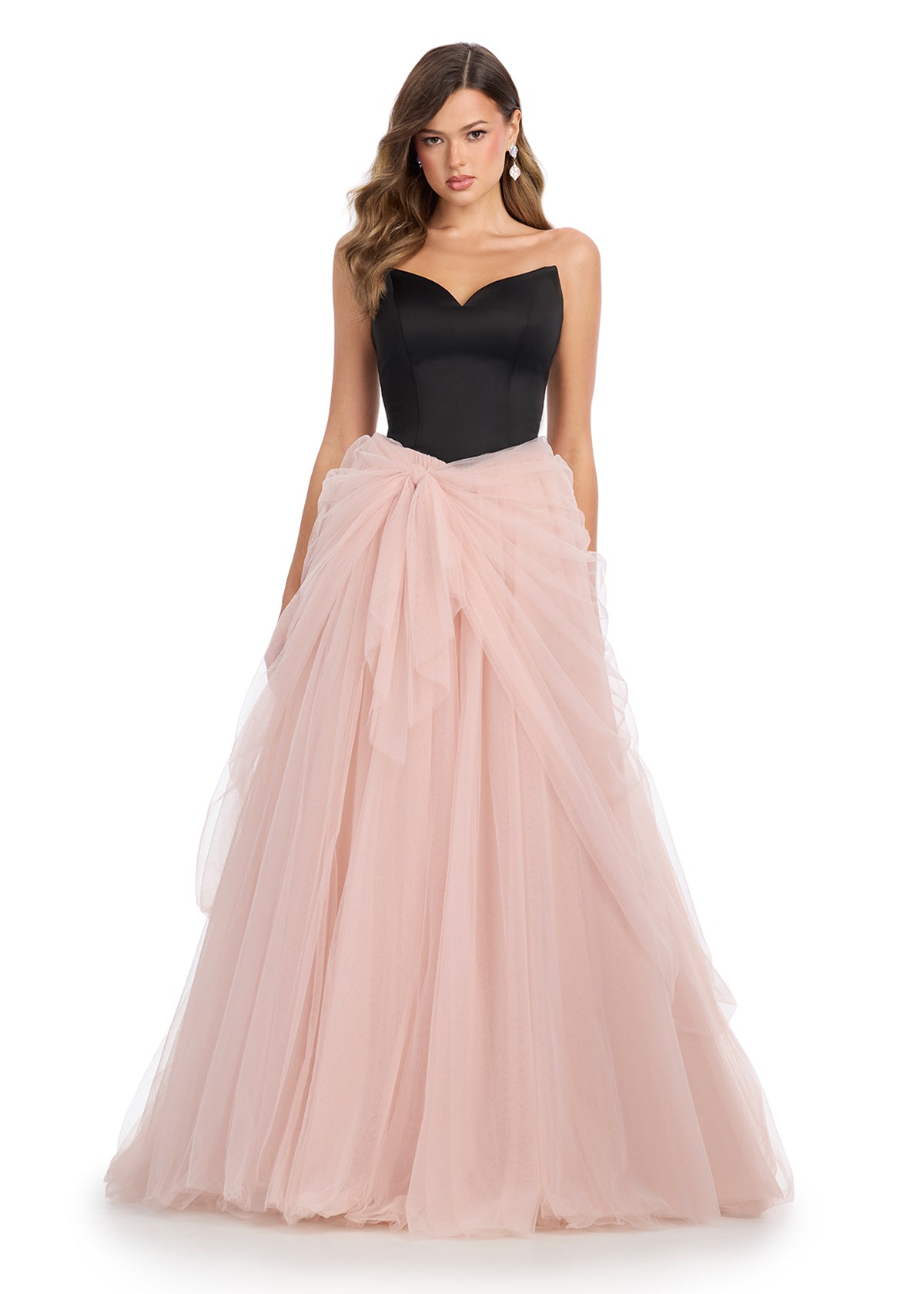 Strapless gown with a fitted black bodice and a voluminous blush pink tulle skirt tied with a flowing bow detail.