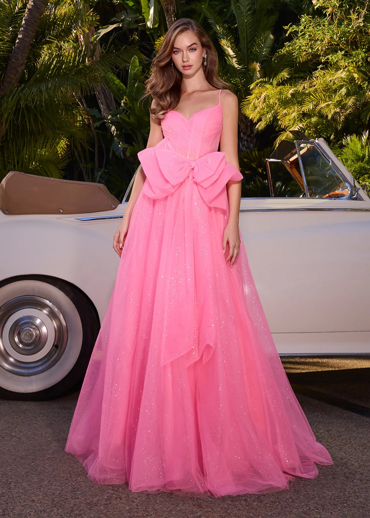 Hot pink tulle ball gown with delicate spaghetti straps, a sheer corset bodice, and an oversized bow accent for a fairytale-inspired look.