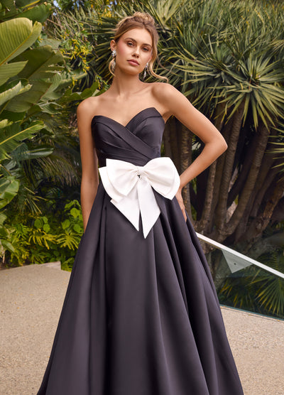 Video - Strapless black ball gown featuring a pleated bodice, a statement oversized bow at the waist, and a dramatic full skirt with a floor-length design.