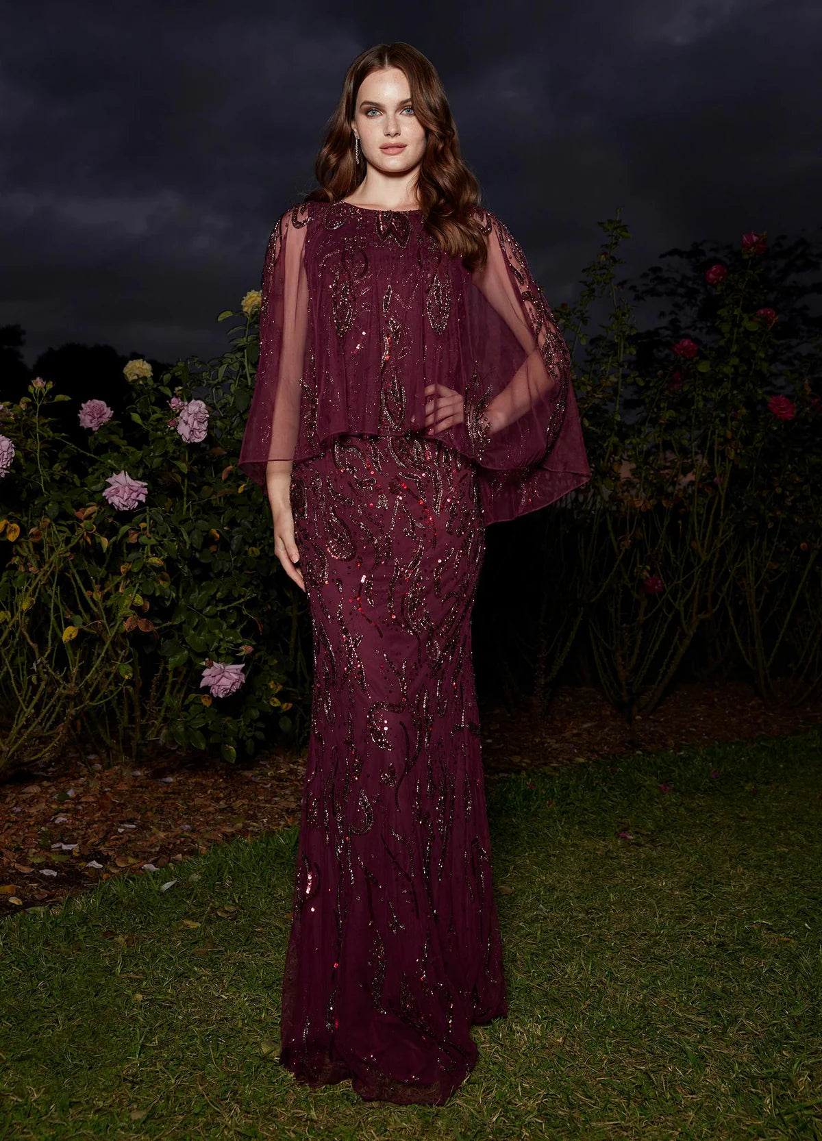 Video - Elegant plum evening gown with a beaded design, sheer cape-style overlay, and a floor-length silhouette for a refined and sophisticated look.